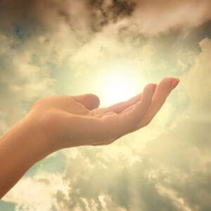 A person 's hand is open in the air with the sun shining.
