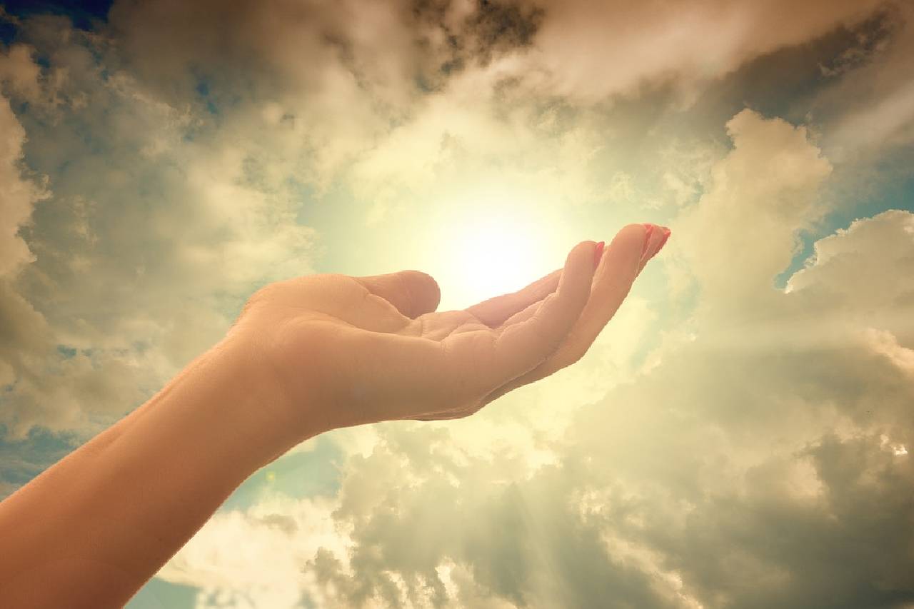 A person 's hand is open in the air with the sun shining.