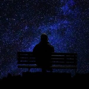 A person sitting on top of a bench under a night sky.