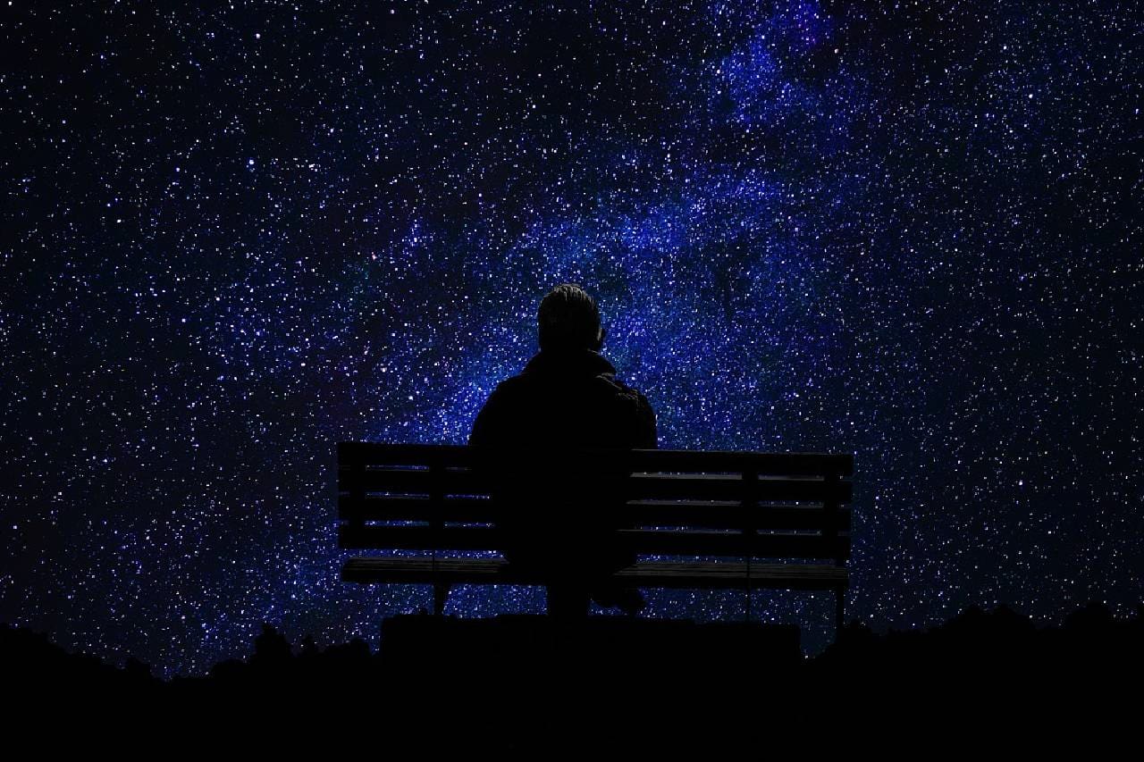 A person sitting on top of a bench under a night sky.
